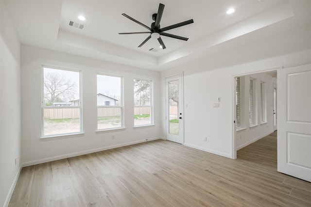 spare room with light hardwood / wood-style floors, a raised ceiling, and ceiling fan