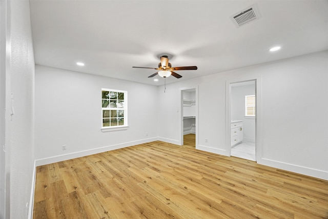 unfurnished bedroom with ceiling fan, a walk in closet, connected bathroom, and light hardwood / wood-style floors