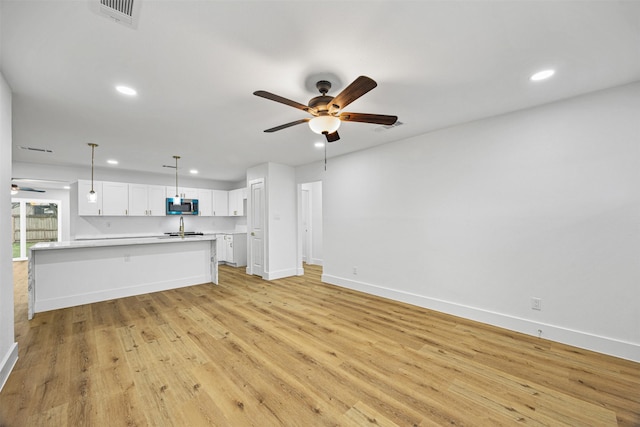 unfurnished living room featuring ceiling fan, sink, and light wood-type flooring