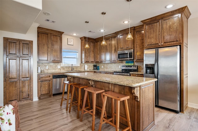 kitchen featuring a center island, hanging light fixtures, light stone countertops, appliances with stainless steel finishes, and light hardwood / wood-style floors