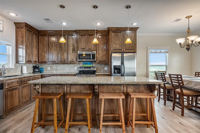 kitchen featuring pendant lighting, a center island, light stone countertops, stainless steel appliances, and a chandelier