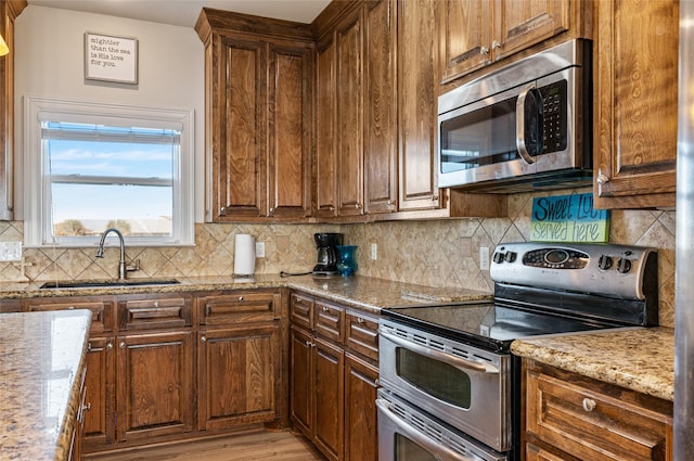 kitchen with decorative backsplash, appliances with stainless steel finishes, light stone counters, sink, and light hardwood / wood-style floors