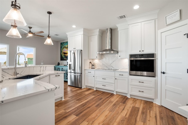 kitchen featuring sink, white cabinets, wall chimney range hood, and appliances with stainless steel finishes