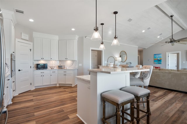 kitchen with backsplash, white cabinetry, a center island with sink, and decorative light fixtures