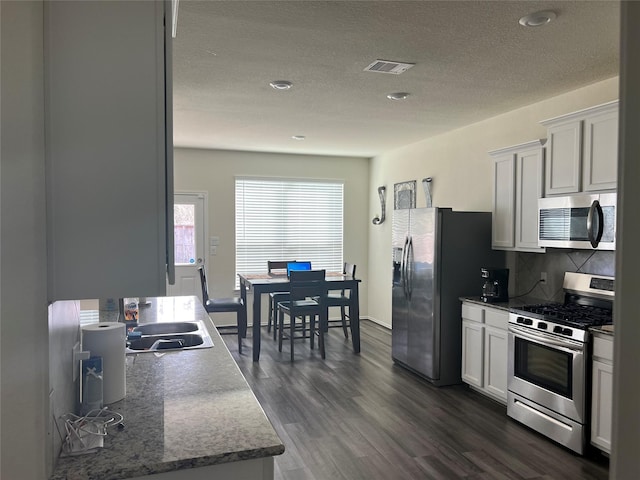 kitchen with dark wood-type flooring, appliances with stainless steel finishes, decorative backsplash, and white cabinetry