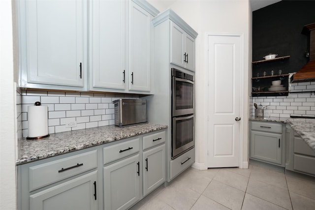 kitchen featuring decorative backsplash, stainless steel double oven, light stone countertops, and light tile patterned flooring