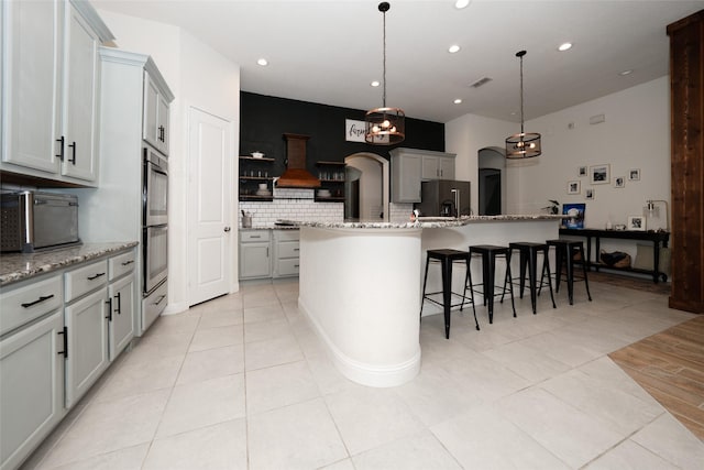 kitchen featuring stainless steel fridge, a kitchen island with sink, pendant lighting, and light stone counters