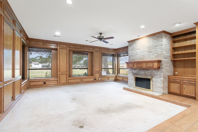 unfurnished living room with a fireplace, ceiling fan, wooden walls, and light carpet