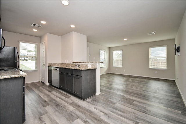 kitchen with stainless steel dishwasher, black refrigerator, light stone countertops, and light hardwood / wood-style floors