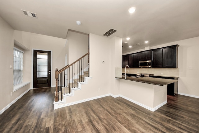 kitchen with tasteful backsplash, appliances with stainless steel finishes, dark hardwood / wood-style floors, and kitchen peninsula