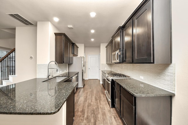 kitchen featuring appliances with stainless steel finishes, light hardwood / wood-style floors, sink, and dark stone countertops