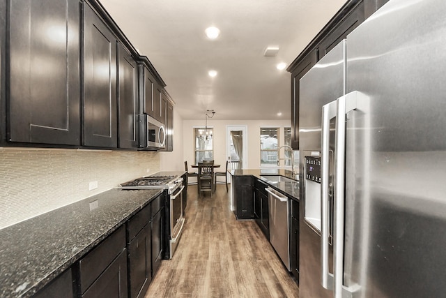 kitchen with sink, hanging light fixtures, light hardwood / wood-style flooring, appliances with stainless steel finishes, and dark stone counters