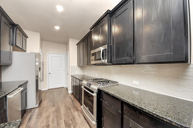 kitchen with tasteful backsplash, appliances with stainless steel finishes, dark stone countertops, and light wood-type flooring