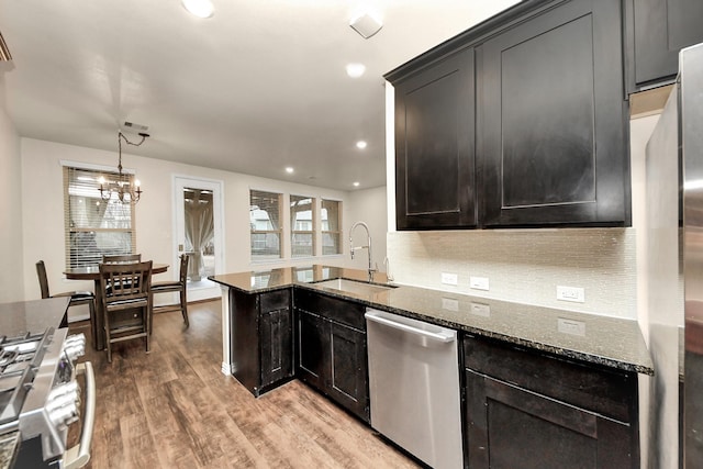 kitchen with pendant lighting, sink, hardwood / wood-style flooring, appliances with stainless steel finishes, and dark stone countertops