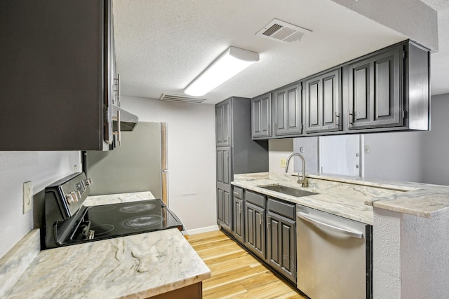 kitchen featuring light wood-style flooring, appliances with stainless steel finishes, light stone countertops, a textured ceiling, and a sink