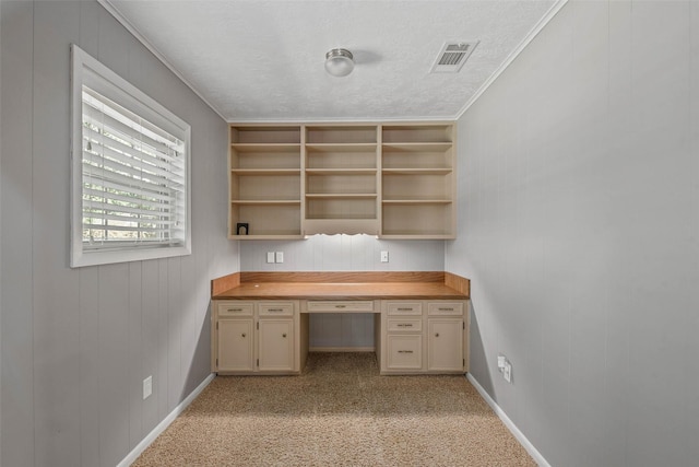 unfurnished office with light carpet, ornamental molding, a textured ceiling, wooden walls, and built in desk