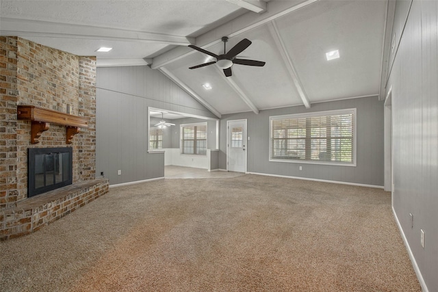 unfurnished living room featuring lofted ceiling with beams, wood walls, light colored carpet, a textured ceiling, and a fireplace