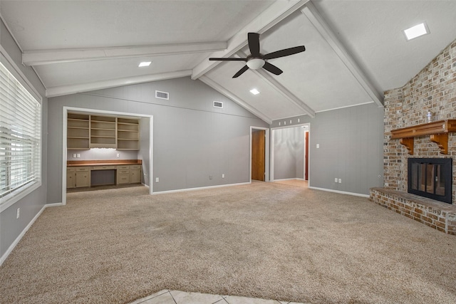 unfurnished living room featuring a brick fireplace, light colored carpet, ceiling fan, lofted ceiling with beams, and built in desk