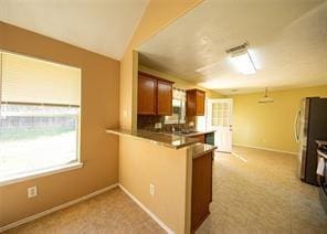 kitchen featuring stainless steel refrigerator, kitchen peninsula, and vaulted ceiling