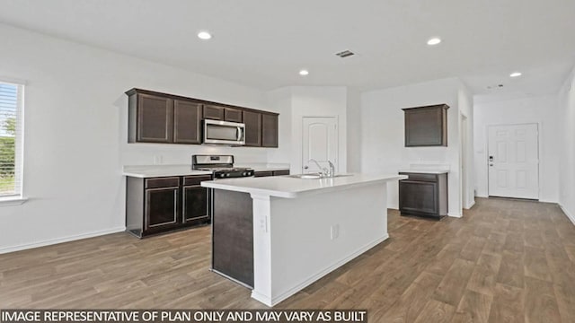 kitchen with hardwood / wood-style floors, dark brown cabinetry, a center island with sink, and stainless steel appliances