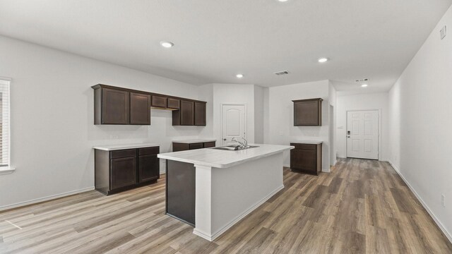 kitchen featuring a kitchen island with sink, light wood-style floors, a sink, and dark brown cabinets