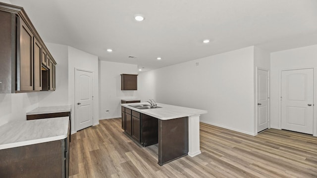 kitchen featuring a sink, light countertops, light wood-type flooring, an island with sink, and dark brown cabinets
