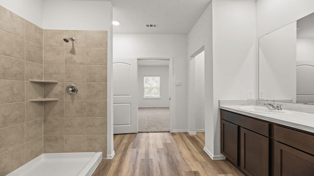 full bath with a tile shower, vanity, visible vents, wood finished floors, and baseboards