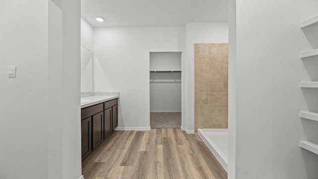 full bath featuring a spacious closet, a stall shower, vanity, and wood finished floors