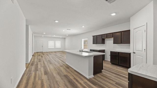 kitchen featuring a center island with sink, a sink, dark brown cabinets, and wood finished floors