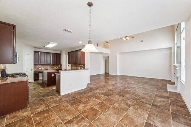 kitchen with stove, backsplash, dark brown cabinets, ceiling fan, and pendant lighting