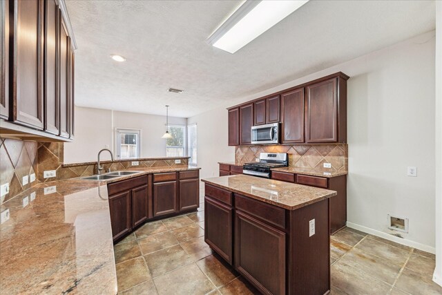 kitchen with light stone countertops, sink, kitchen peninsula, decorative light fixtures, and appliances with stainless steel finishes