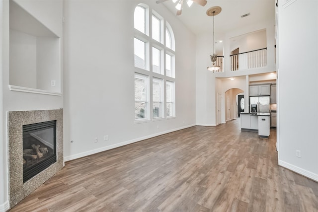 unfurnished living room featuring a high ceiling, a tiled fireplace, ceiling fan, and light hardwood / wood-style flooring