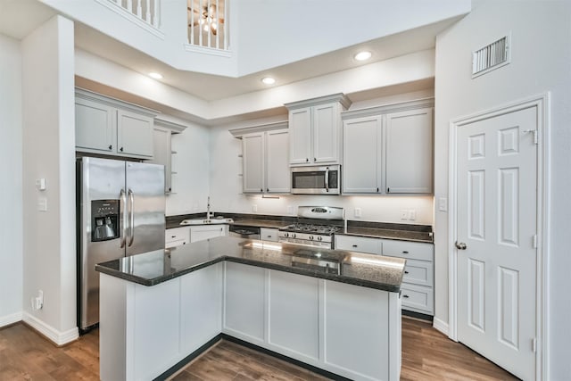 kitchen featuring gray cabinets, appliances with stainless steel finishes, a center island, dark stone counters, and dark wood-type flooring