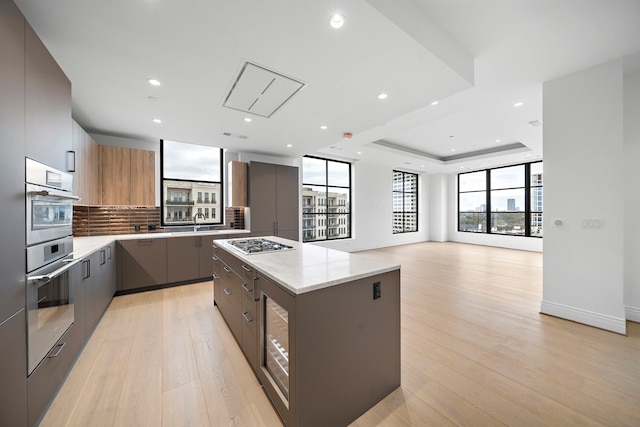 kitchen with a center island, a raised ceiling, light stone countertops, appliances with stainless steel finishes, and tasteful backsplash