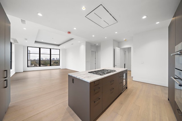 2323 San Felipe St Unit 803, Houston, TX 77019 - kitchen with light stone countertops, a raised ceiling, stainless steel gas cooktop, light hardwood / wood-style flooring, and a kitchen island