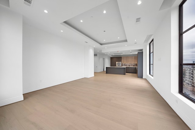 unfurnished living room featuring light hardwood / wood-style floors and a tray ceiling