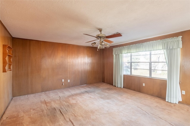 carpeted spare room featuring ceiling fan, wood walls, and a textured ceiling