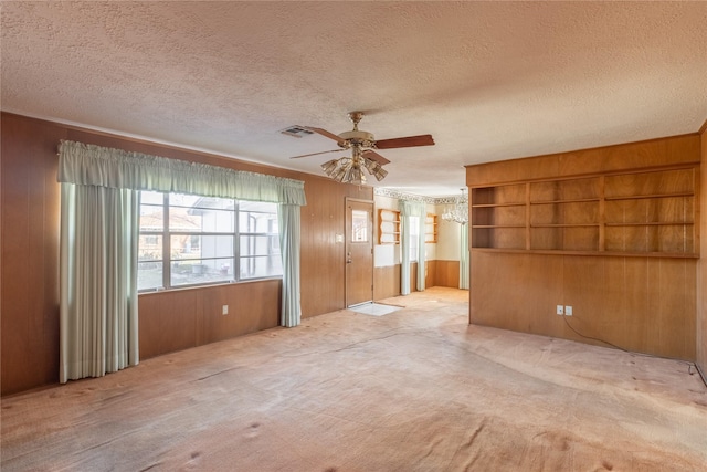 carpeted spare room featuring wooden walls, ceiling fan, and a textured ceiling