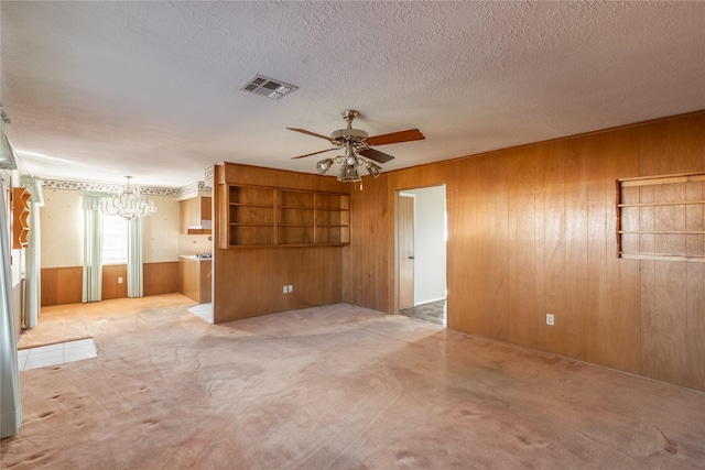 unfurnished living room featuring a textured ceiling, wood walls, light colored carpet, and ceiling fan with notable chandelier