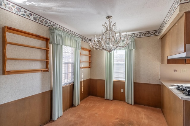 unfurnished dining area featuring plenty of natural light, light colored carpet, a textured ceiling, and a notable chandelier