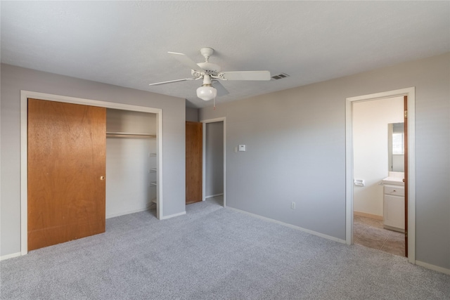 unfurnished bedroom featuring light carpet, a closet, ensuite bathroom, and ceiling fan