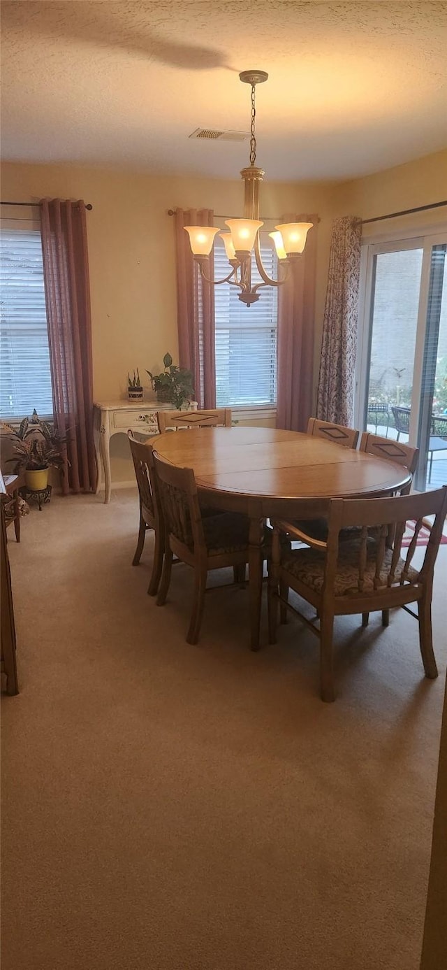 carpeted dining space featuring plenty of natural light, a chandelier, and a textured ceiling