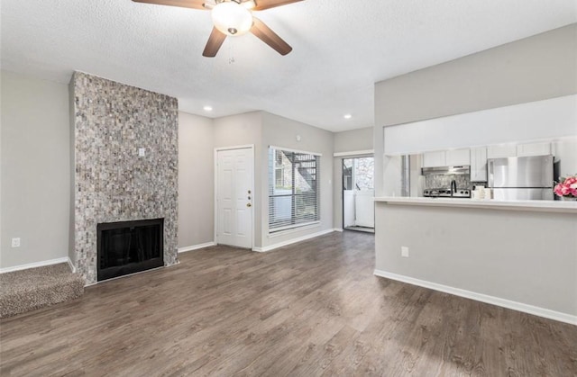 unfurnished living room featuring dark wood-type flooring, ceiling fan, a fireplace, and a textured ceiling