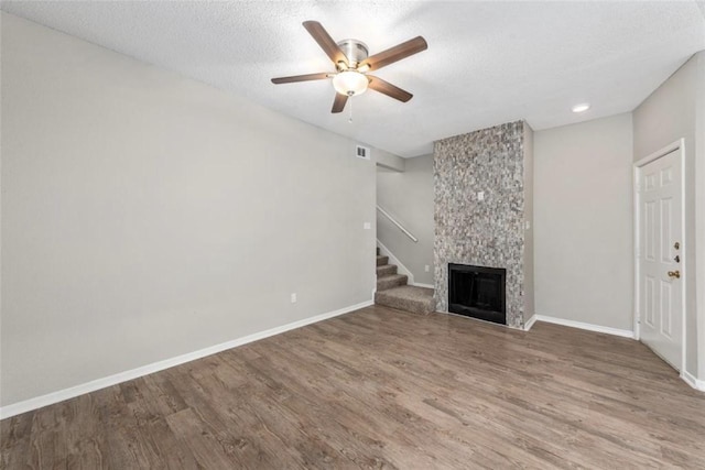 unfurnished living room featuring ceiling fan, wood-type flooring, a fireplace, and a textured ceiling