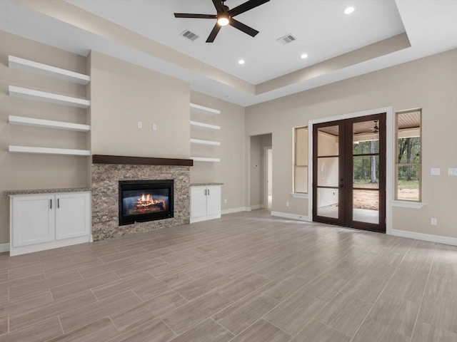 unfurnished living room with a raised ceiling, a fireplace, ceiling fan, and french doors