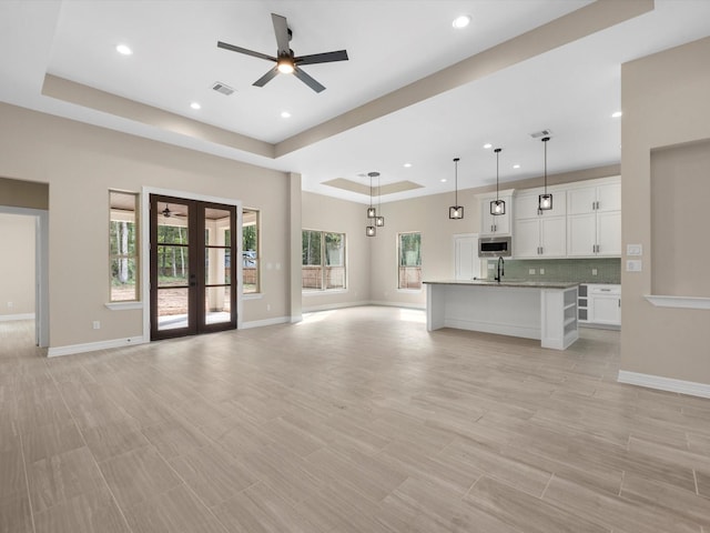 unfurnished living room with a tray ceiling, ceiling fan, french doors, and plenty of natural light