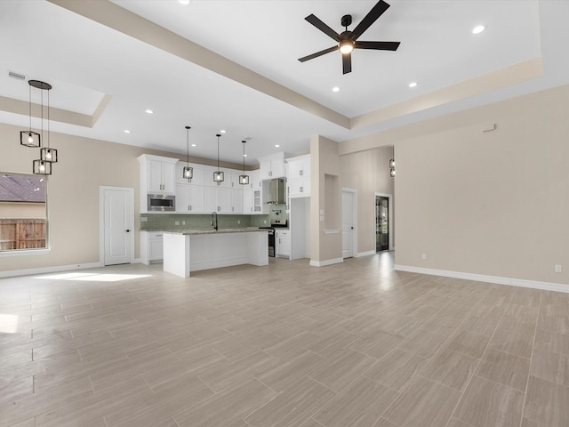 unfurnished living room with ceiling fan, a raised ceiling, sink, and a wealth of natural light