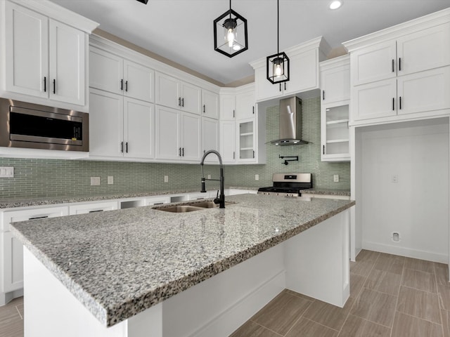 kitchen with white cabinetry, sink, wall chimney exhaust hood, stainless steel appliances, and a kitchen island with sink