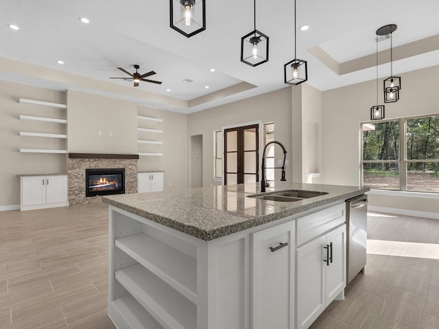 kitchen featuring a raised ceiling, a kitchen island with sink, sink, and hanging light fixtures