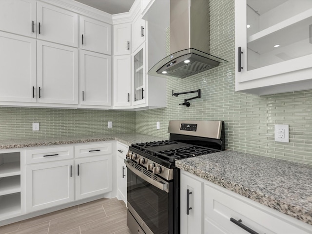 kitchen featuring decorative backsplash, light stone countertops, stainless steel gas range oven, wall chimney exhaust hood, and white cabinets